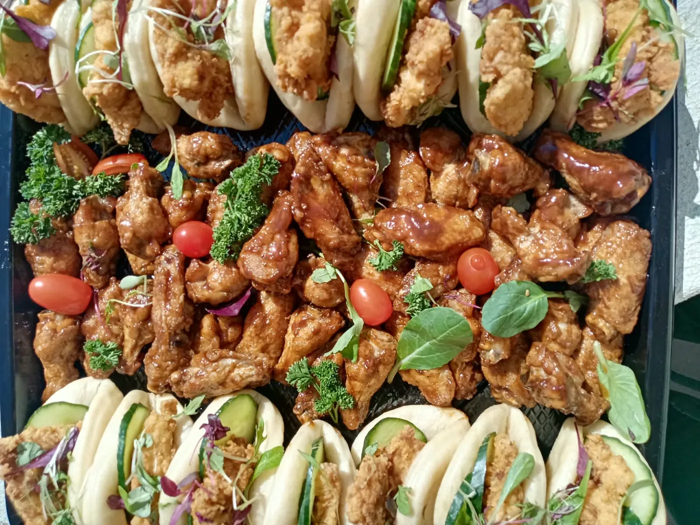 Bao buns filled with crumbed chicken and cucumber, framing a bed of sticky glazed wings